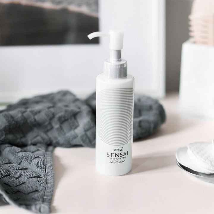 Sensai Silky Purifying Milky Soap Step 2 fuktighetsgivende ansiktsrens i hvit pumpeflaske ved en grå klut.