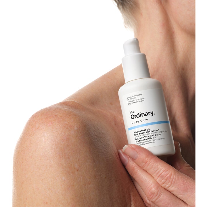The Ordinary Niacinamide 5% Face & Body Emulsion 100 ml i hvit pumpeflaske holdt mot en skulder.