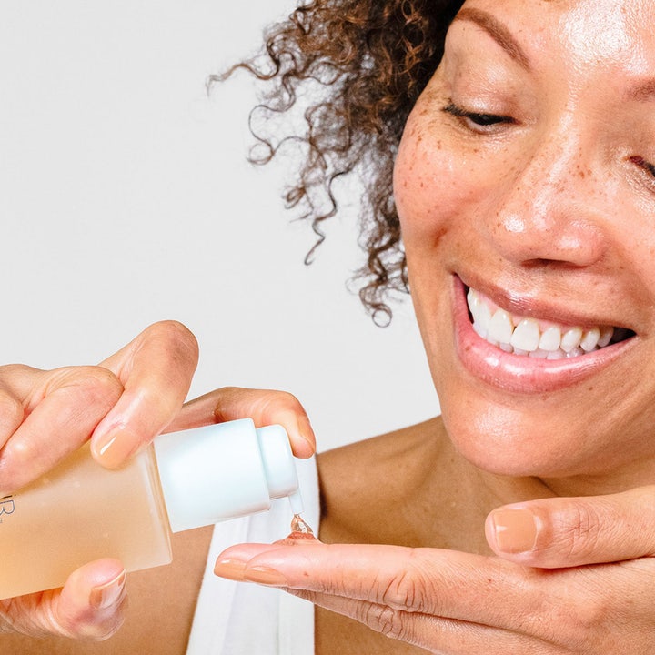 PÜR Ceratin Booster Age Defying Retinol Serum 30 ml anti-aging hudpleie som en kvinne pumper på hånden fra en frostet flaske