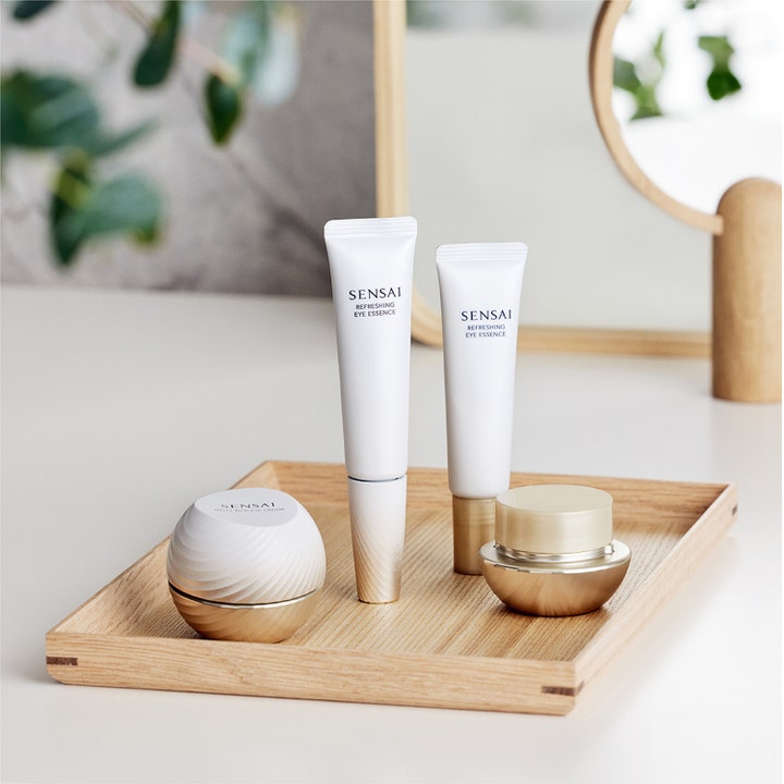 Sensai Total Eye Treatment 35 ml øyekrem og essence i hvite og gullfargede beholdere på et trebrett