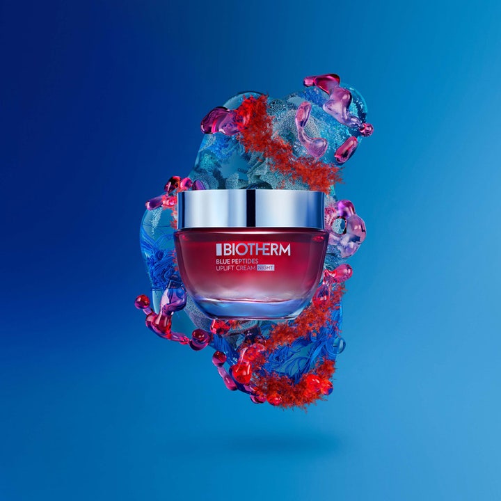 Biotherm Blue Peptides Uplift 50 ml nattkrem i rød glasskrukke med sølvlokk mot en blå abstrakt bakgrunn.