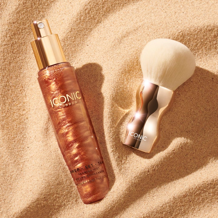 ICONIC London Prep Set Tan 75 ml selvbruning spray som gir glød ved siden av gullfarget kost på sand