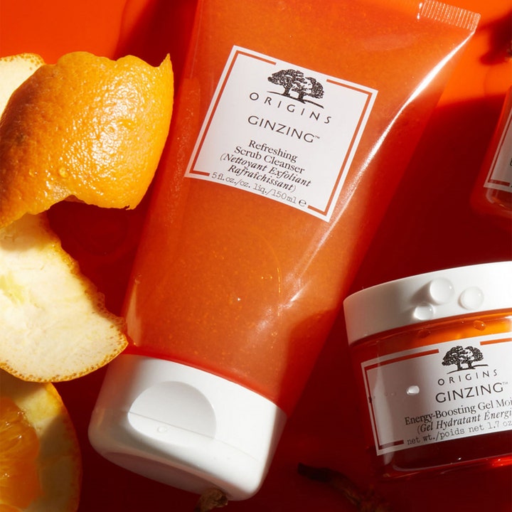 Origins GinZing Refreshing Scrub Cleanser 150 ml ansiktsskrubb i oransje tube ved siden av ferskt appelsinskall