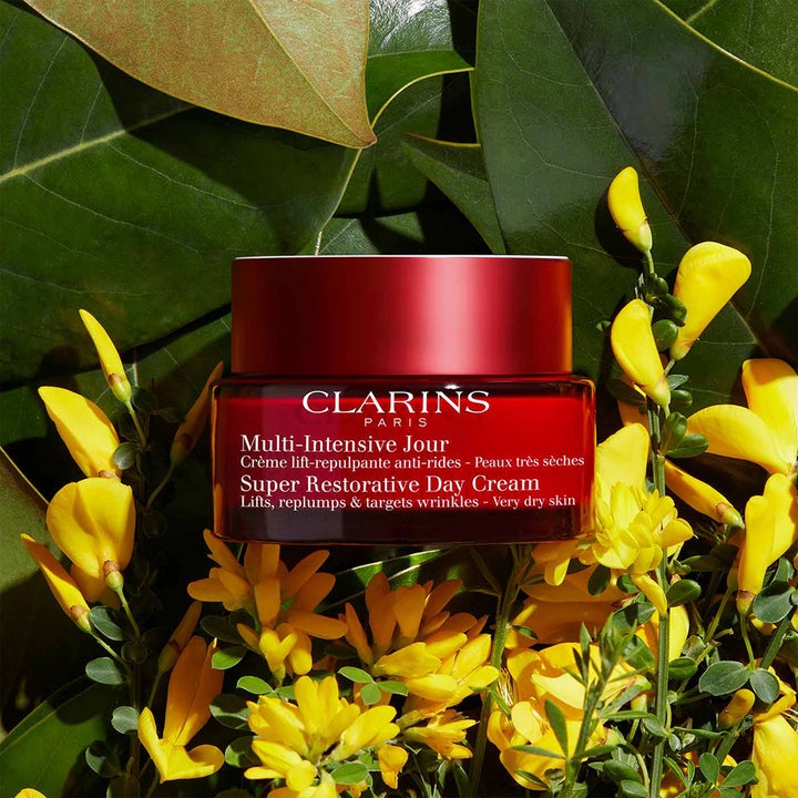 Clarins Super Restorative Day Cream 50 ml pleiende dagkrem i rød glasskrukke blant gule blomster og blader