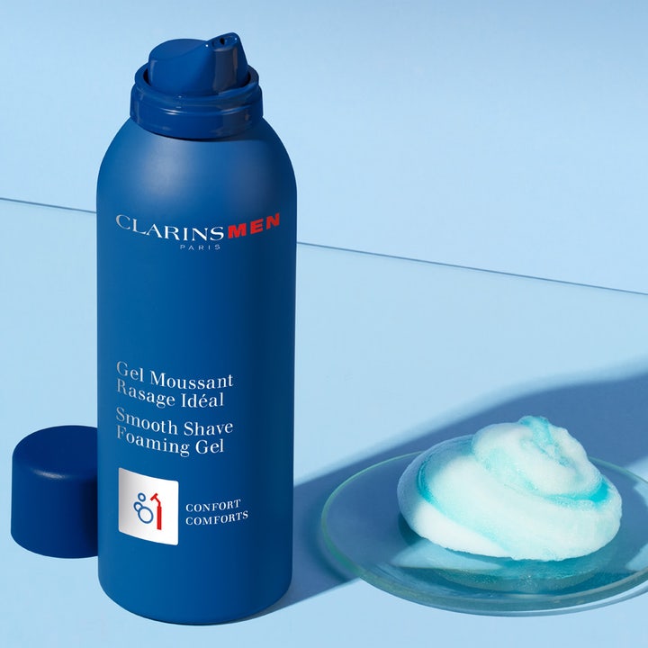 Clarins Men Shave Gel 150 ml rakgel for behagelig barbering vist som blå sprayflaske og luftig blåhvitt skum.