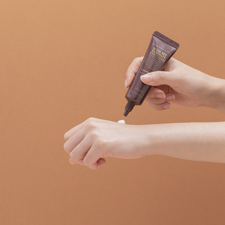 Benton Snail Bee Ultimate Eye Cream 30 g påføres fra brun tube på håndryggen for glødende hud.
