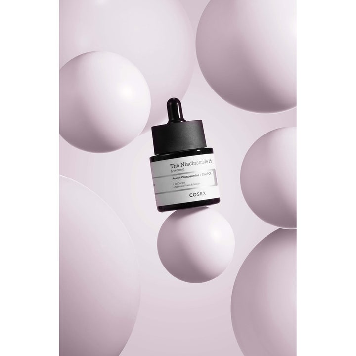 COSRX The Niacinamide 15 Serum 20 ml ansiktsserum mot porer i mørk glassflaske omgitt av lilla sfærer