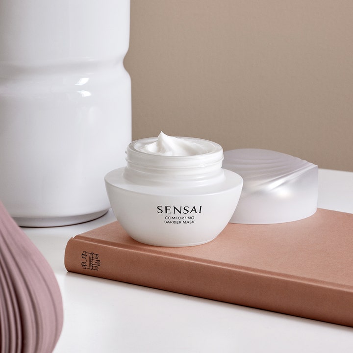 Sensai Comforting Barrier Mask 60 ml styrkende ansiktsmaske i hvit krukke med synlig kremet tekstur på en bok