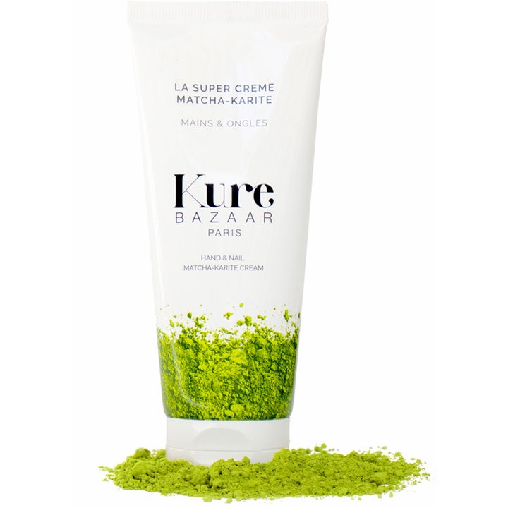 Kure Bazaar La Super Creme Matcha-Karite pleiende håndkrem i hvit tube stående i en haug med grønt matchapulver.