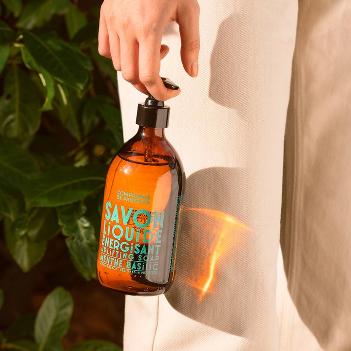 Compagnie de Provence Liquid Marseille Soap Mint Basil 495 ml i brun glassflaske holdt av en hånd i sollys.