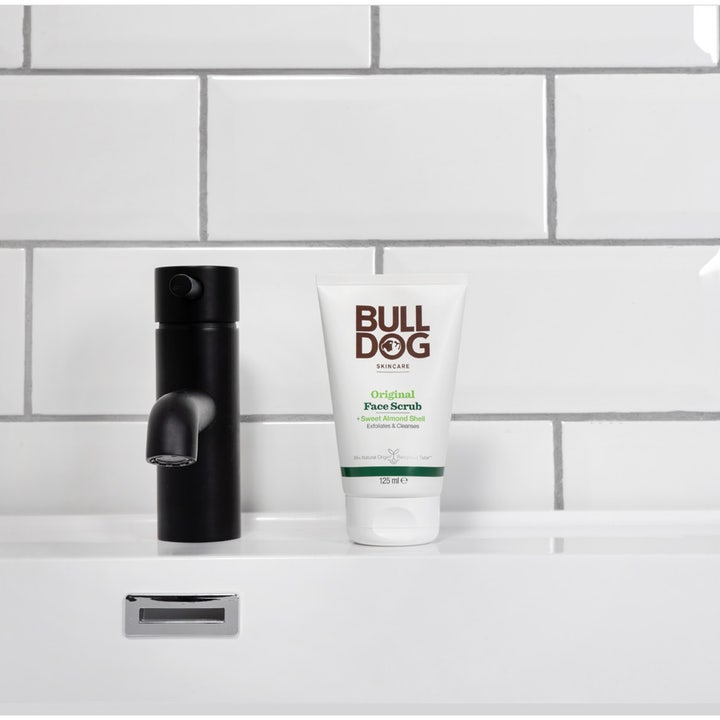 Bulldog Original Face Scrub 125 ml eksfolierende ansiktsskrubb i hvit tube ved en svart kran på baderommet.