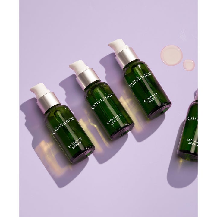 Exuviance Radiance Serum 30 ml glødgivende ansiktsserum i grønne glassflasker med hvit pumpe og dråper av tekstur