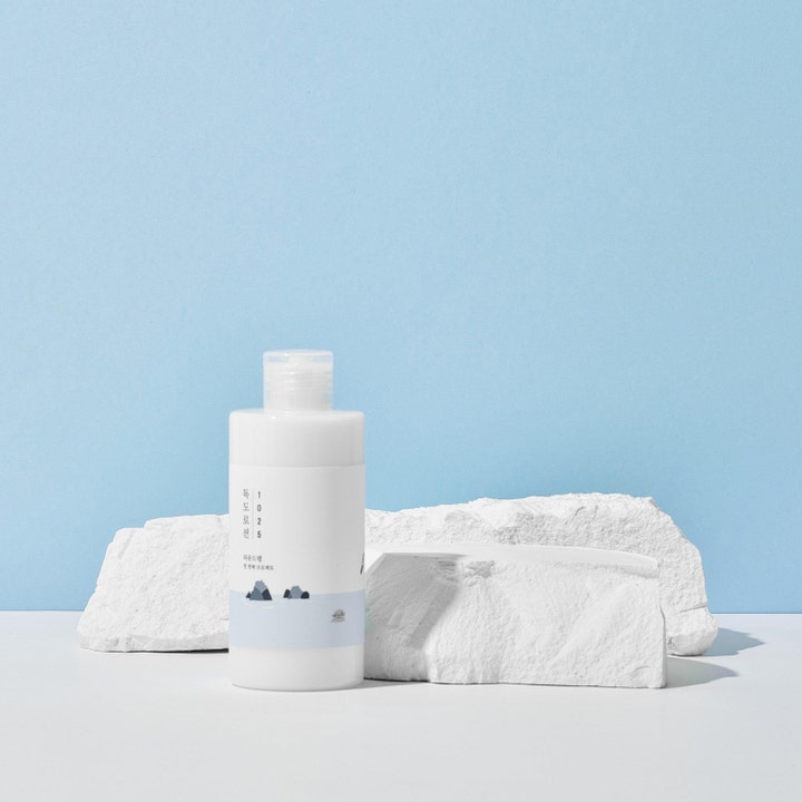 Round Lab 1025 Dokdo Lotion fuktighetskrem i hvit plastflaske plassert foran hvite dekorsteiner