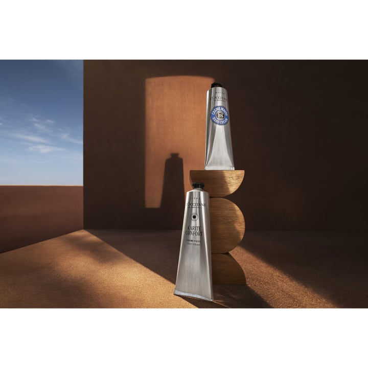 L'Occitane Shea Butter Foot Cream 150 ml fotkrem på sølvtube i en kunstnerisk setting med treskulpturer