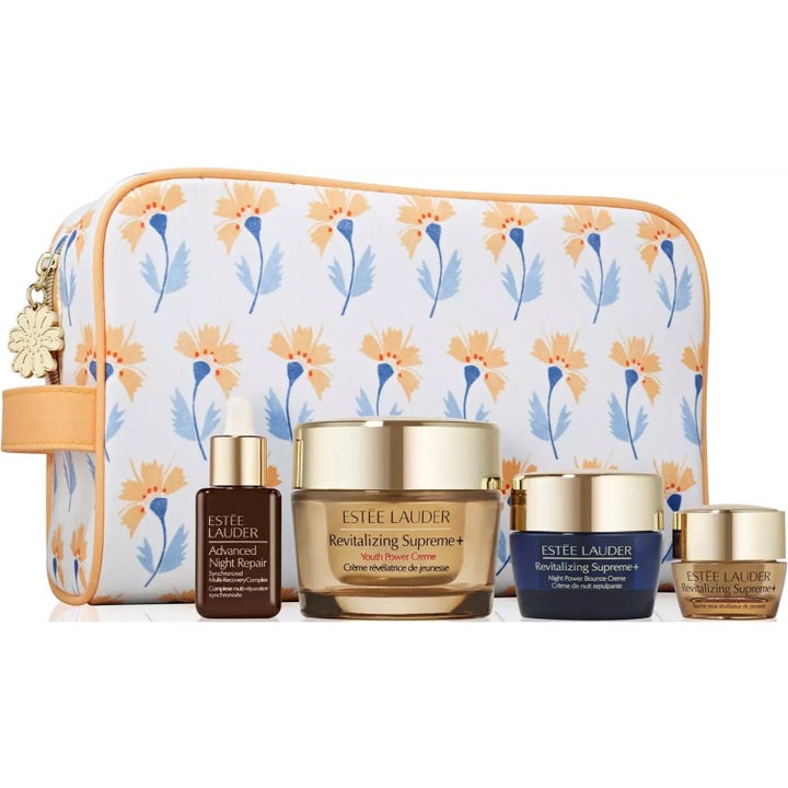 Estée Lauder Revitalizing Supreme+ gaveesett gir glød med krukker i gull og blått foran en hvit blomstret toalettmappe.
