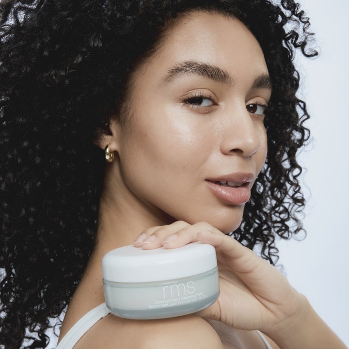 RMS Beauty Coconut Clean Cleansing Balm 100 g ansiktsrengjøring i glasskrukke holdt av kvinne med krøller