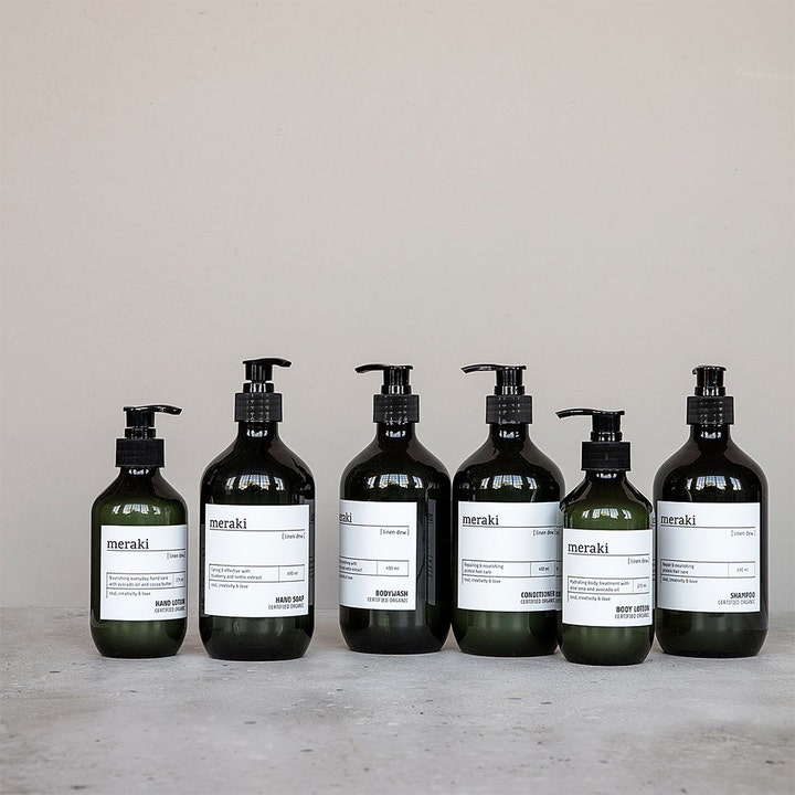 Meraki Linen Dew Hand Soap 490 ml pleiende håndsåpe i mørkebrune pumpeflasker på en rustikk grå overflate.