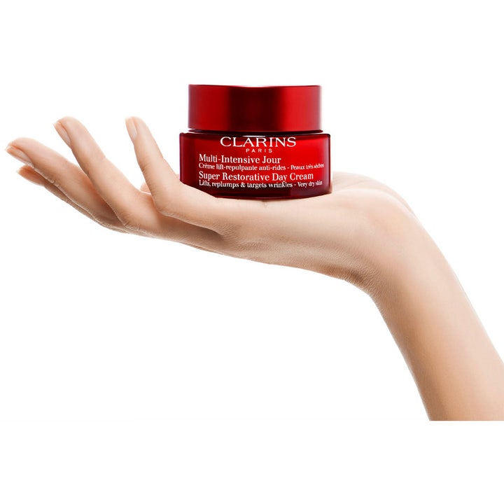 Clarins Super Restorative Day Cream 50 ml gjenoppbyggende dagkrem i rød krukke som holdes i en åpen håndflate.