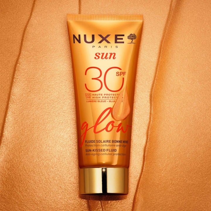 Nuxe Sun-Kissed Fluid SPF 30 40 ml solkrem for ansiktet i oransje tube mot en glitrende bakgrunn
