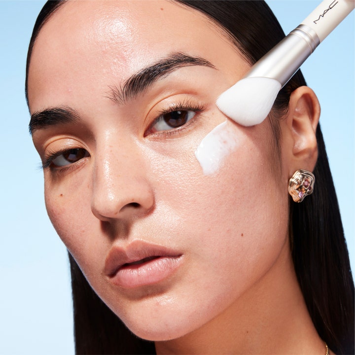 MAC Cosmetics Serum + Moisturizer Brush 1 stk hudpleiebørste påfører en hvit fuktighetskrem på kinnet til en modell.