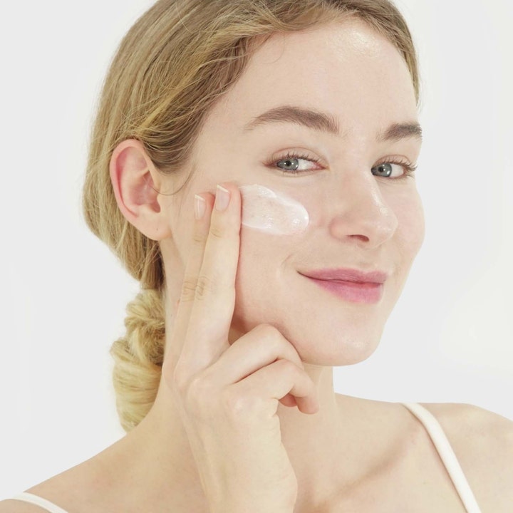 Purito Dermide Relief Barrier Moisturizer 100 ml beroligende ansiktskrem påføres av en kvinne med hvit krem på kinnet