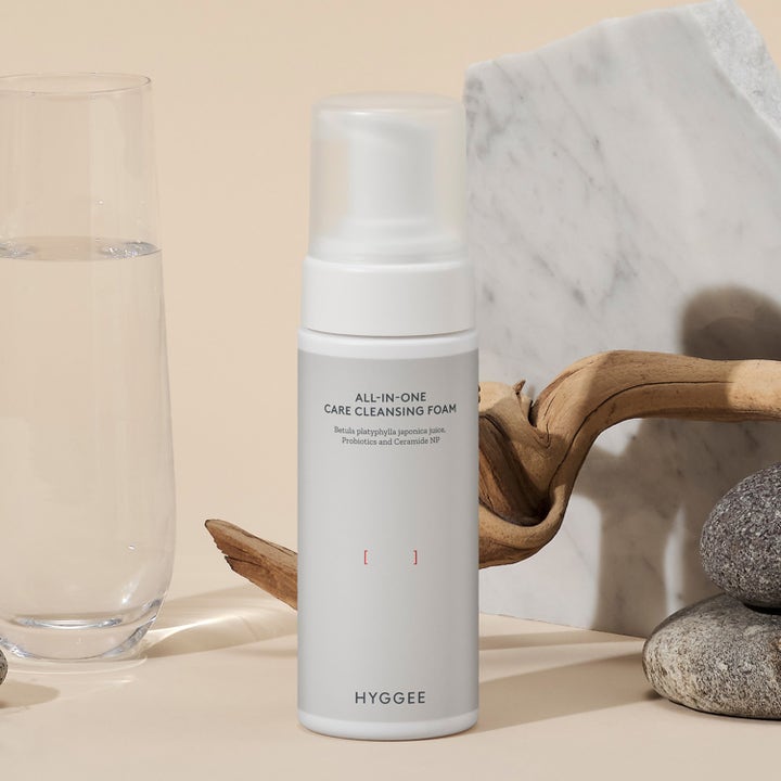 Hyggee All-In-One Care Cleansing Foam 150 ml ansiktsrengjøring i hvit pumpeflaske ved siden av marmor og vann