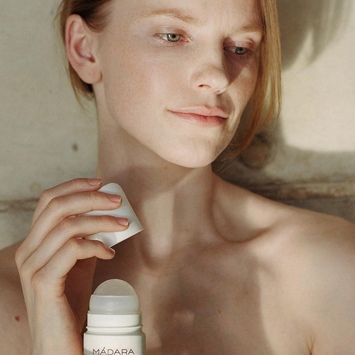 MÁDARA Herbal Deodorant 50 ml roll-on som gir friskhet i en livsstilssetting med en kvinne som holder produktet.