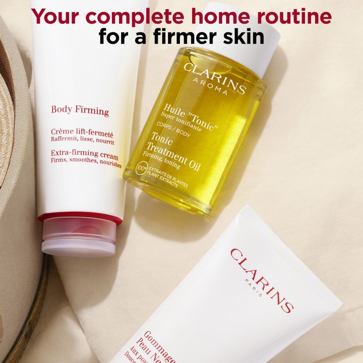 Clarins Body Firming Extra-Firming Cream 200 ml i hvit tube ved siden av gul kroppsolje for fastere hud.