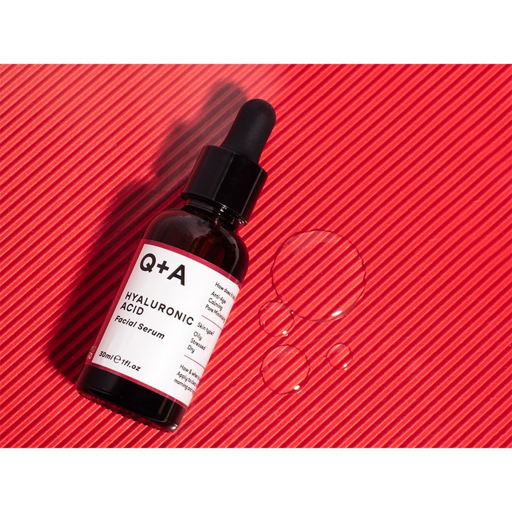 Q+A Hyaluronic Acid Facial Serum 30 ml fuktighetsgivende hyaluronsyreserum i glassflaske med dråper på rød bakgrunn.