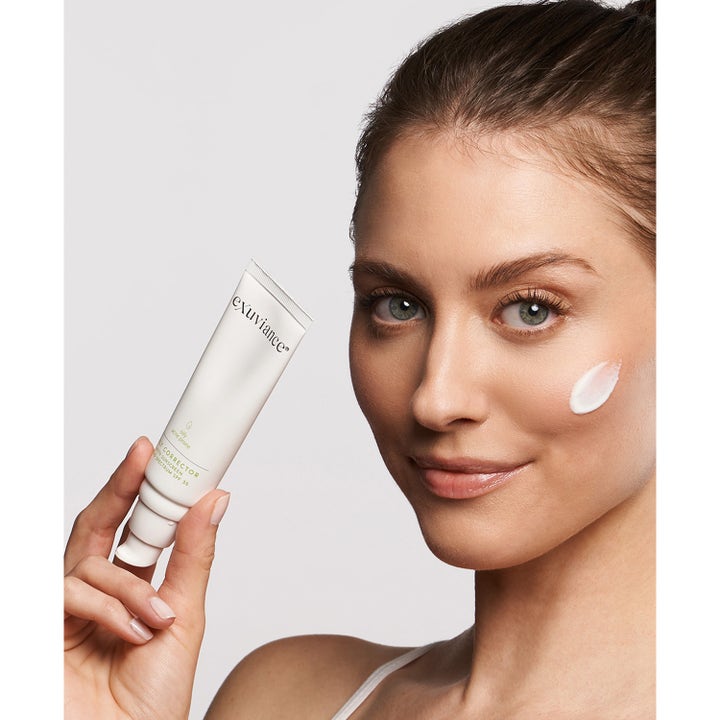 Exuviance Daily Corrector 40 g solkrem for ansiktet SPF 35 i hvit tube påført som en dert på kvinnes kinn.