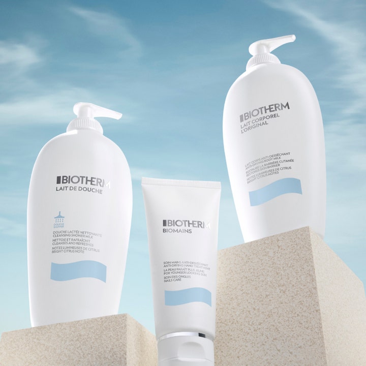 Biotherm Lait Corporel 400 ml fuktighetsgivende kroppspleie i hvite flasker plassert på steiner mot blå himmel