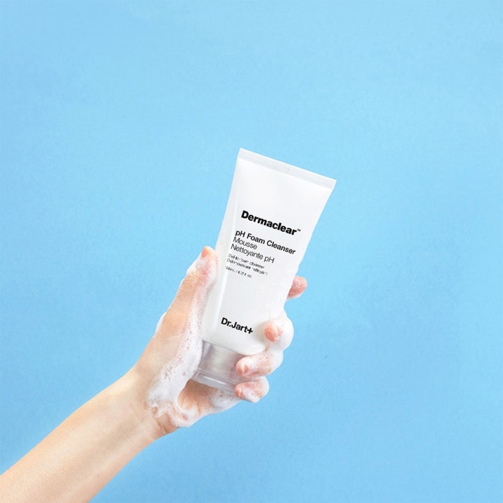 Dr.Jart+ Dermaclear pH Foam Cleanser 120 ml ansiktsrengjøring i hvit tube holdt av en hånd dekket med hvitt skum.