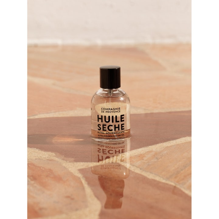 Compagnie de Provence Ultra Nourishing Dry Oil Shea Butter 100 ml pleiende kroppsolje i glassflaske på stein.