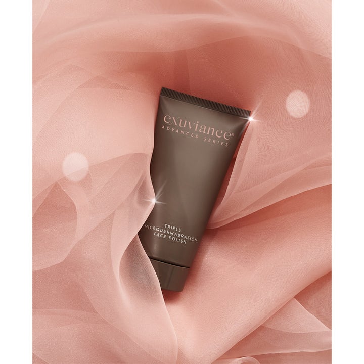 Exuviance Triple Microdermabrasion Face Polish 75 g eksfolierende peeling i brun tube på rosa, luftig stoff
