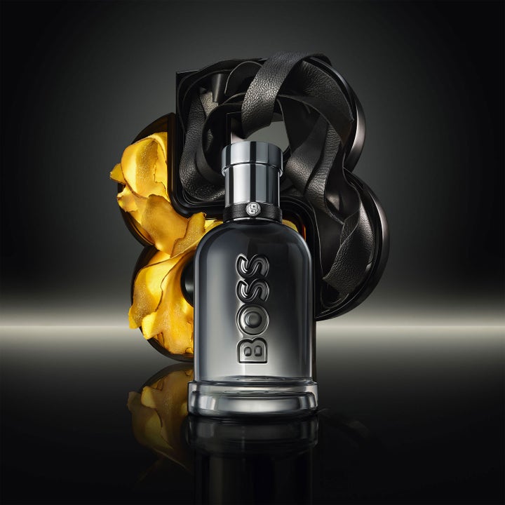 Hugo Boss Bottled Beyond Shower Gel 200 ml dusjsåpe i mørk flaske foran dekorative gullblader og svarte lærreimer.
