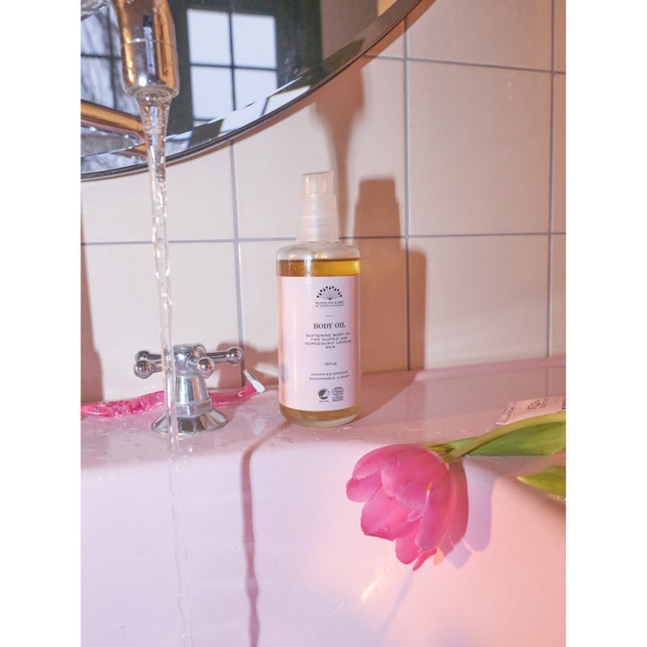 Rudolph Care Acai Body Oil 200 ml mykgjørende kroppsolje i pumpeflaske ved en rosa vask med en rosa tulipan