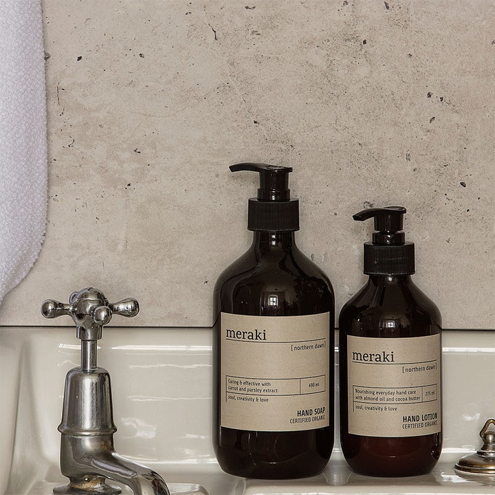Meraki Northern Dawn Hand Lotion 275 ml pleiende håndkrem i brun pumpeflaske ved siden av en vask