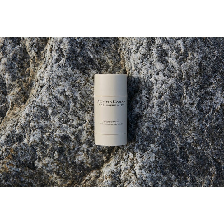 DKNY Cashmere Mist Deostick motvirker fukt i en beige hylse plassert på en teksturert grå steinoverflate.