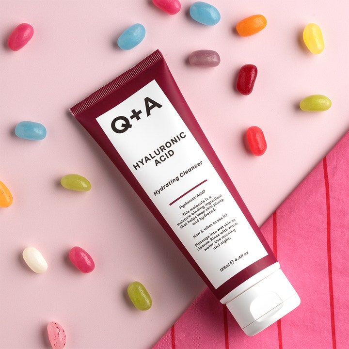 Q+A Hyaluronic Acid Gel Cleanser 125 ml fuktighetsgivende ansiktsrens i burgunderrød tube omgitt av fargerike gelébønner
