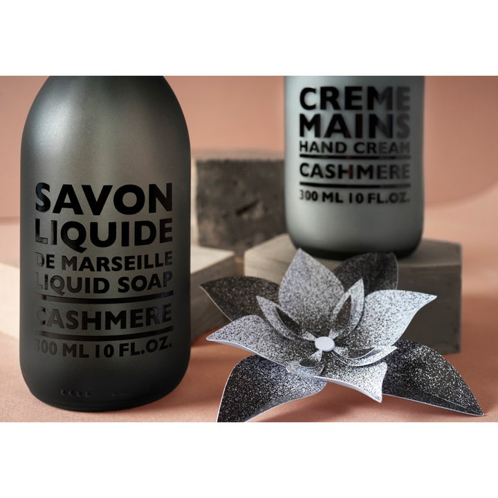 Compagnie de Provence Liquid Marseille Soap Cashmere 300 ml håndsåpe i matt mørkegrå flaske ved en dekorativ papirblomst.