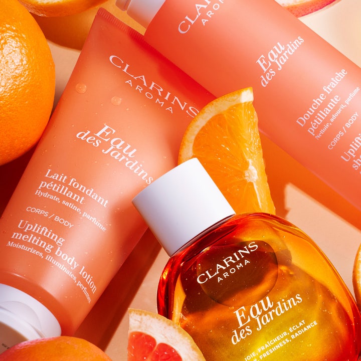 Clarins Eau des Jardins 200 ml oppløftende dusjsåpe i oransje tube omgitt av friske appelsinskiver og sitrus