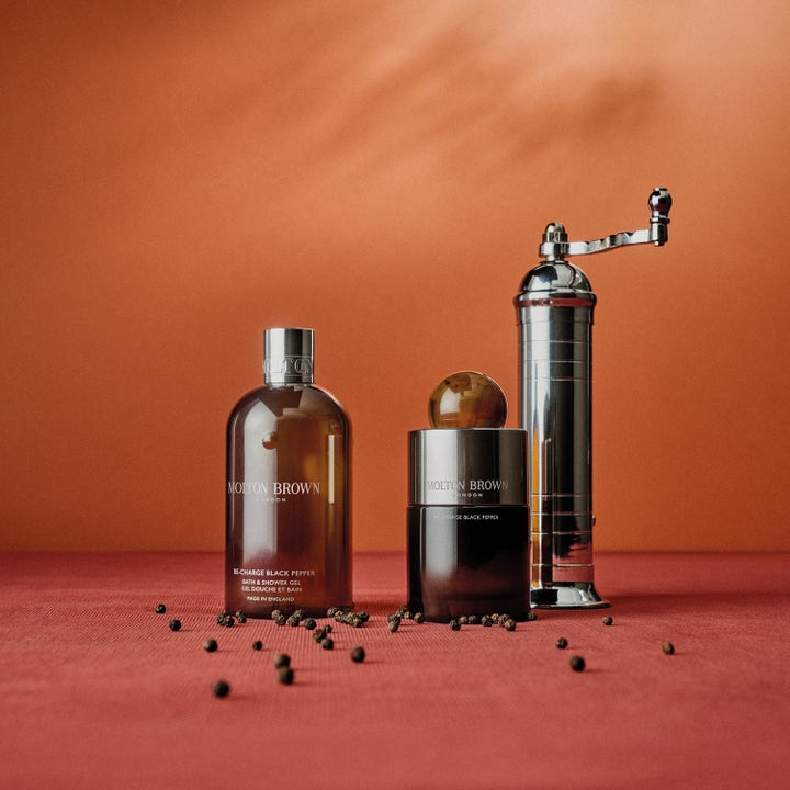 Molton Brown Black Peppercorn Body Wash 300 ml dusjsåpe ved en sølvfarget pepperkvern og spredte sorte pepperkorn.