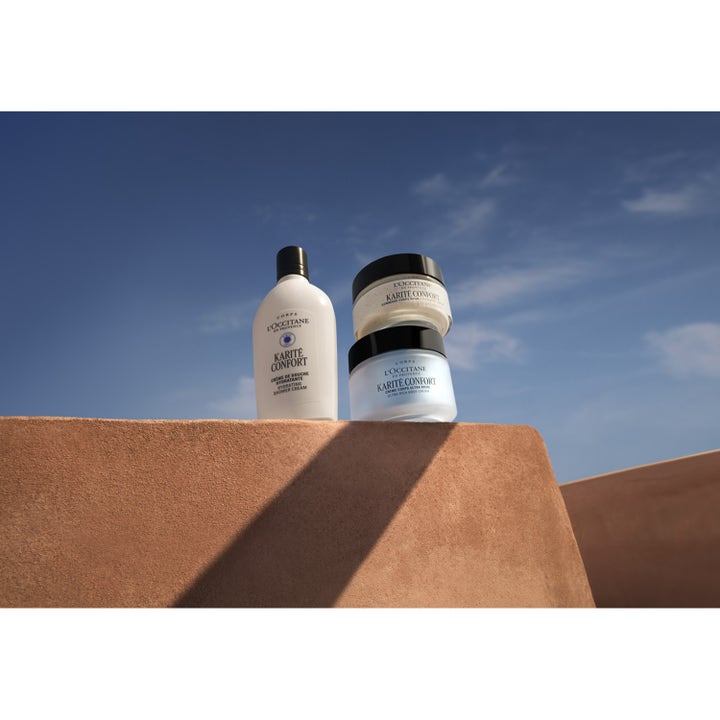L'Occitane en Provence Shea Butter Rich Body Scrub 200 ml eksfolierende krukke med sort lokk i sollys mot blå himmel