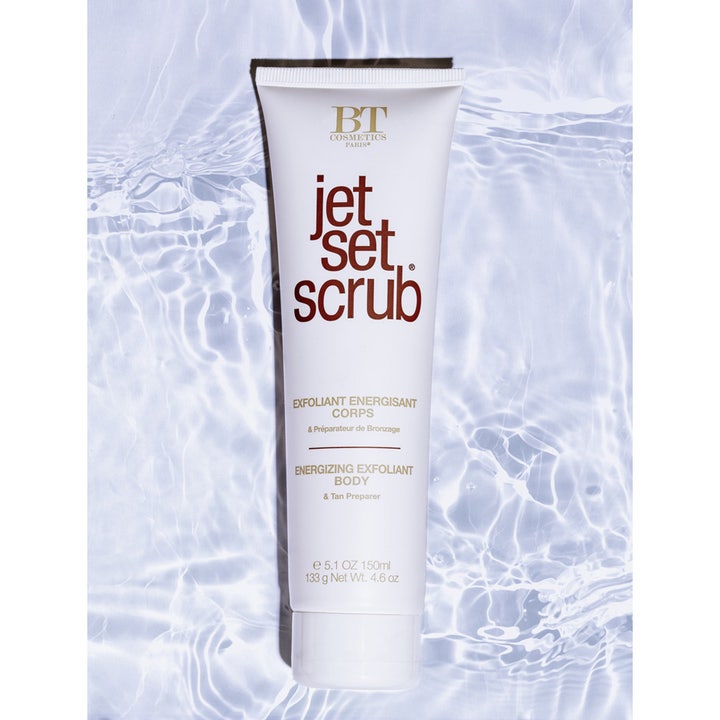 Jet Set Sun Jet Set Scrub Body 150 ml eksfolierende kroppsskrubb i hvit tube på en bakgrunn av lyseblått vann