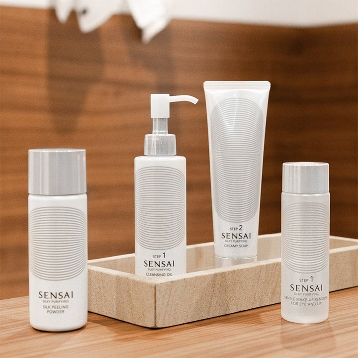 Sensai Silky Purifying Cleansing Oil ansiktsrengjøring i hvit pumpeflaske på et steinbrett sammen med hudpleiesett