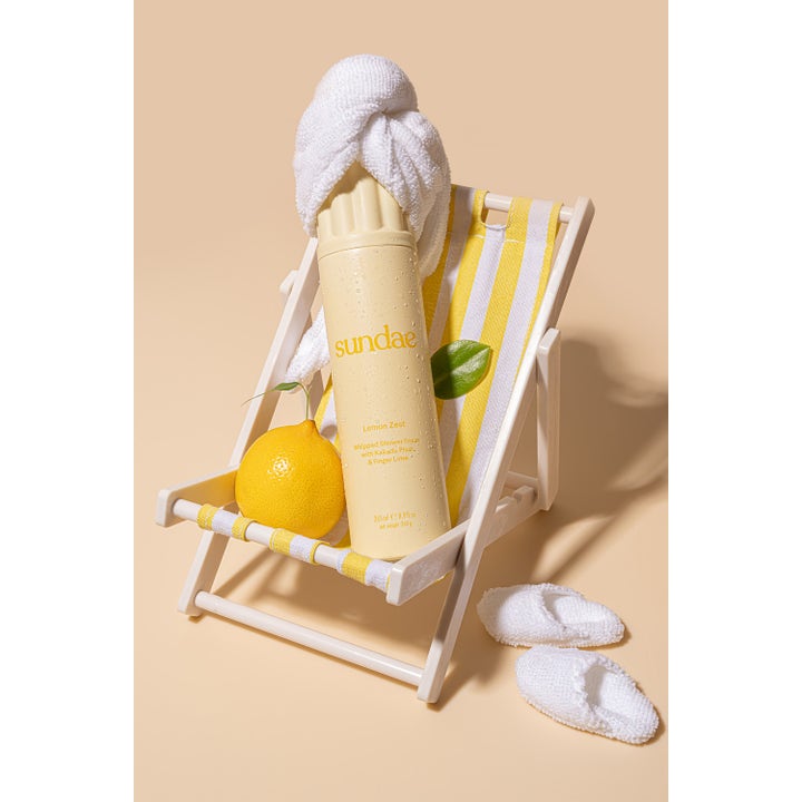 Sundae Whipped Shower Foam Lemon Zest 265 ml forfriskende dusjsåpe i gul flaske i en liten fluktstol med sitron.