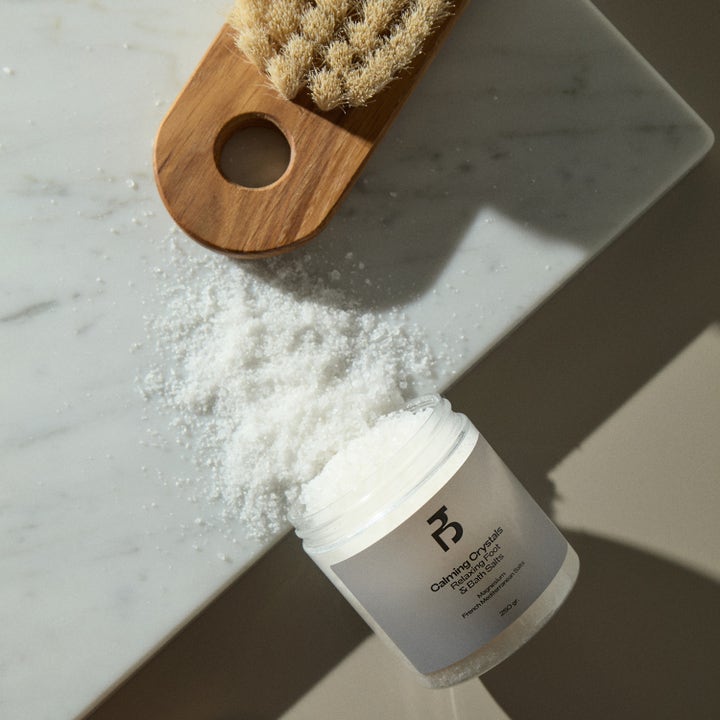 Bodyologist Calming Crystals 250 g avslappende badesalt helt ut på marmor ved en trehårbørste
