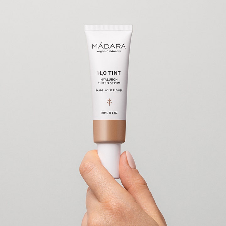 MÁDARA H2O Tint Hyaluron Tinted Serum 30 ml fuktgivende serum i hvit tube som holdes i en hånd
