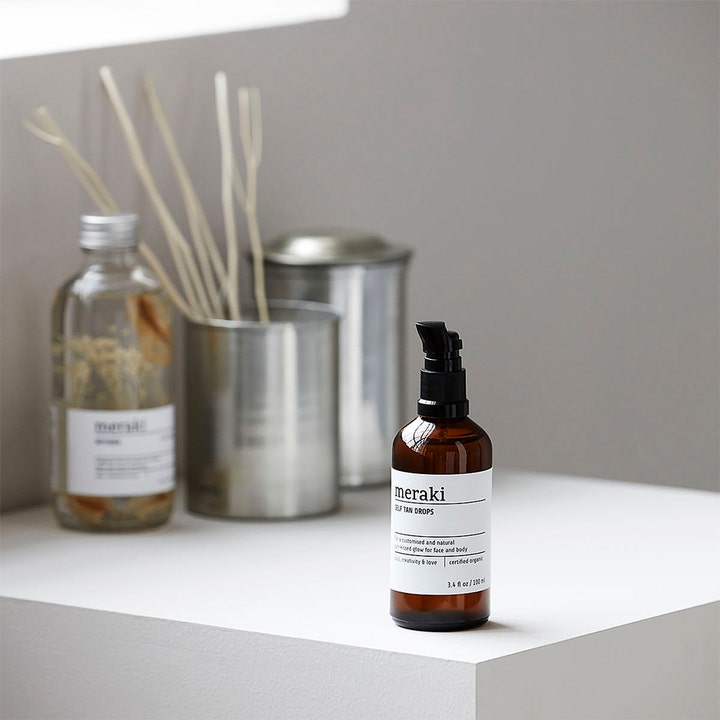 Meraki Self Tan Drops 100 ml selvbruning som gir naturlig glød i en brun glassflaske med sort pumpe.