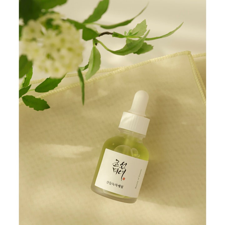 Beauty of Joseon Calming Serum 30 ml beroligende ansiktsserum i glassflaske ved siden av hvite blomster og blader.